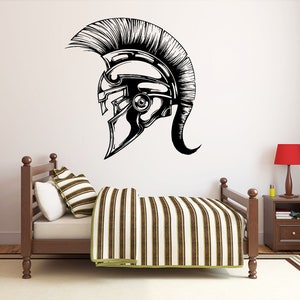 May include: A black and white illustration of a Roman helmet with a plume on top. The helmet is on a white wall above a wooden bed with a striped comforter.
