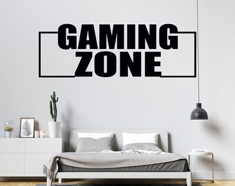 May include: Black and white wall decal with the text "GAMING ZONE" in a rectangular frame. The decal is on a white wall above a bed with gray bedding.