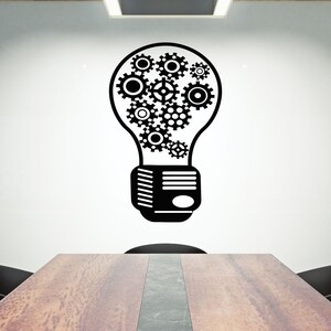 May include: A black and white illustration of a light bulb with gears inside. The light bulb is on a white wall in a conference room with a wooden table and chairs.