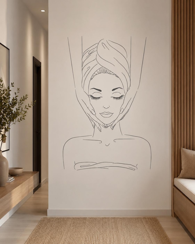 May include: A black line art wall decal featuring a person with eyes closed, wrapped in a towel, receiving a facial massage. The minimalist illustration depicts the head, shoulders, and hands of a practitioner performing the massage treatment.