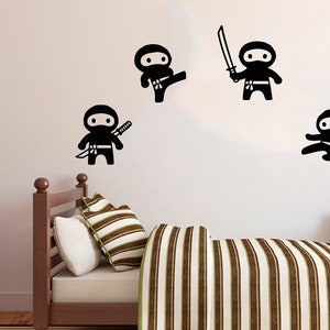 May include: Four black silhouette wall decals of ninjas in various poses, including one holding a sword. The decals are on a white wall above a brown wooden bed with striped bedding.
