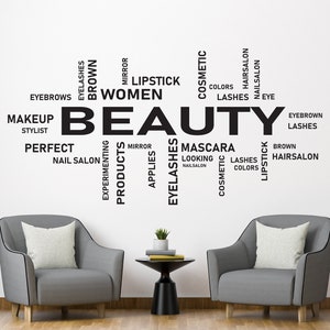 Może przedstawiać: Biała ściana z napisem "BEAUTY" dużymi czarnymi literami otoczona mniejszymi czarnymi słowami związanymi z pięknem i kosmetykami, takimi jak "rzęsy", "szminka", "makijaż" i "salon fryzjerski". Dwa szare fotele z białymi poduszkami znajdują się przed ścianą.