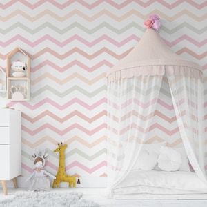 May include: A white canopy bed with a pink and beige chevron patterned fabric. The canopy is made of white tulle and has a pink fabric top with a flower embellishment. The bed is on a white wooden floor.