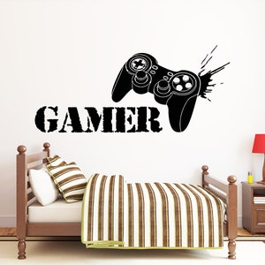 May include: Black and white wall decal of a video game controller with the word "GAMER" underneath. The decal is on a white wall with a bed and nightstand in the background.