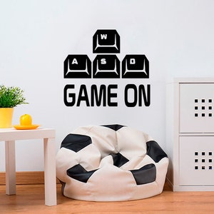 May include: Black and white keyboard keys with the letters W, A, S, and D, and the text "GAME ON" on a white wall. A white beanbag chair with black soccer ball pattern is in the foreground.