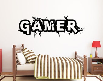 May include: Black and white wall decal with the word "GAMER" in a stylized font. The decal is on a white wall above a wooden bed with a striped comforter.
