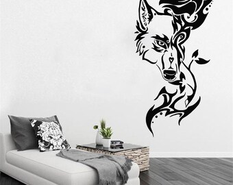 May include: Black and white wall decal of a wolf's head with a rose and tribal design. The decal is on a white wall with a couch and a side table in the background.