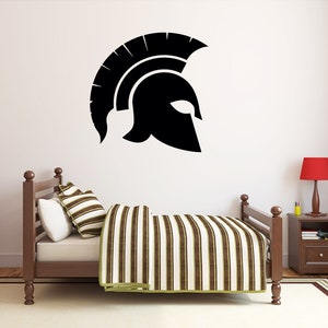 May include: A black and white silhouette of a Spartan helmet on a white wall above a wooden bed with a striped comforter and pillows.