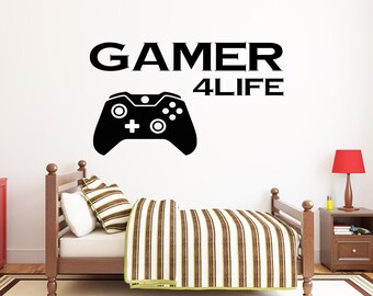 May include: Black and white wall decal with a video game controller and the text "GAMER 4LIFE". The decal is on a white wall above a wooden bed with a striped comforter.
