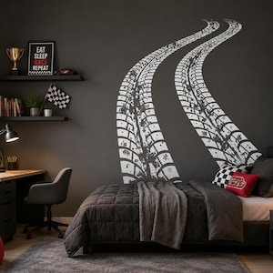May include: A large white wall decal featuring two curved tyre tracks extending vertically across a dark grey wall. The design mimics the appearance of skid marks left by a vehicle, creating a bold graphic element above a bed in a bedroom.
