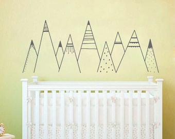 May include: A nursery wall decal featuring a row of gray mountain silhouettes with various patterns, including stripes, dots, and zigzags. The decal is applied to a yellow wall above a white crib.