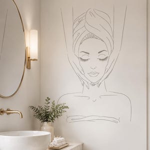May include: A wall decal featuring a minimalist line art illustration of a person with eyes closed, wrapped in a towel, receiving a facial massage. The design is rendered in thin, dark grey lines against a neutral, light-coloured wall surface.