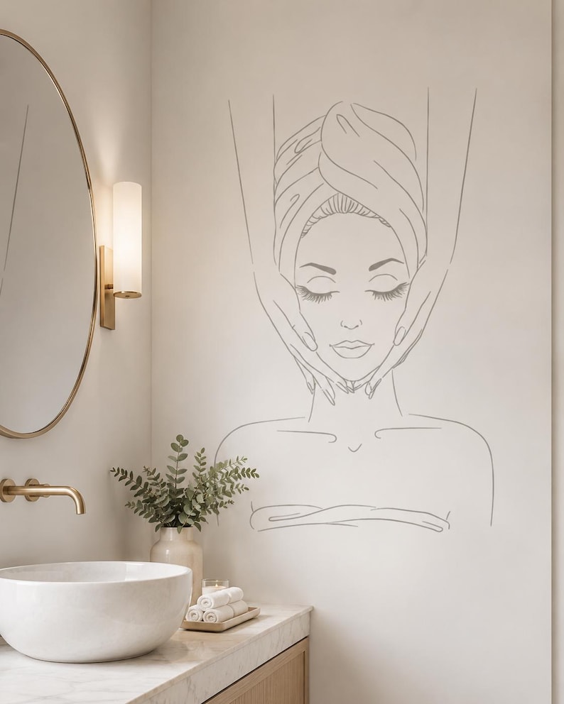 May include: A wall decal featuring a minimalist line art illustration of a person with eyes closed, wrapped in a towel, receiving a facial massage. The design is rendered in thin, dark grey lines against a neutral, light-coloured wall surface.