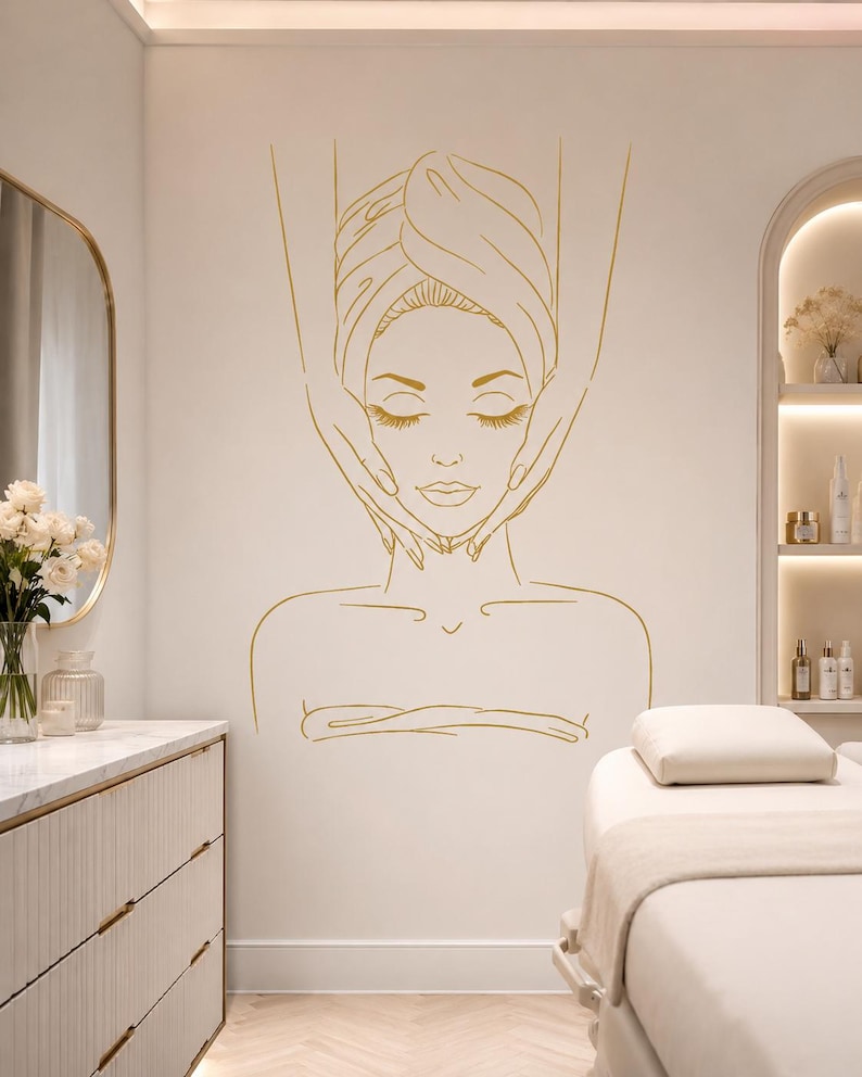 May include: A gold line art wall decal featuring a stylised illustration of a person receiving a facial massage. The design depicts a face with closed eyes, a towel wrapped around the head, and hands positioned on the cheeks and jawline.