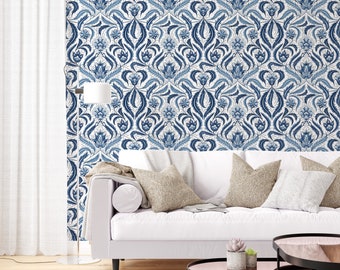 May include: A white couch with blue and white patterned wallpaper in the background. The couch has three pillows, one white, one beige, and one blue. There is a small potted plant on a round table in front of the couch.