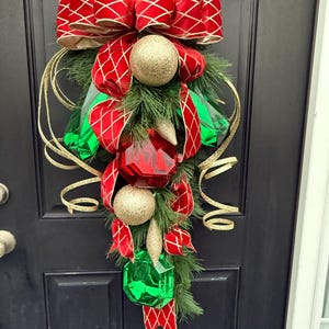 May include: A Christmas door swag with a red and gold bow, green pine branches, and red and green diamond-shaped ornaments.