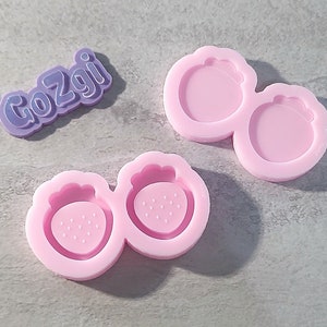 May include: Two pink silicone molds for making strawberry shaped resin crafts. The molds are connected together and have a raised design of a strawberry with seeds.