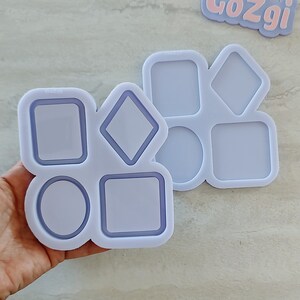 May include: A purple silicone mold with eight different shapes: two squares, two circles, two diamonds, and two rectangles. The mold is labeled "GoZgi".