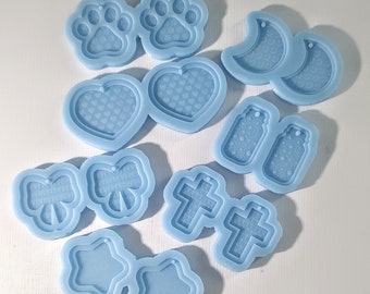May include: A selection of light blue silicone moulds in diverse shapes: paw prints, hearts, moons, tags, bows, crosses, and stars. These moulds are likely for crafting or jewellery making, providing a variety of design choices.