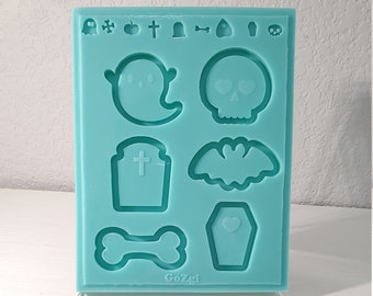May include: A teal blue silicone mould with eight Halloween-themed shapes: a ghost, skull, cross, tombstone, bat, bone, coffin, and a heart. The mould is labelled "Gozgi".