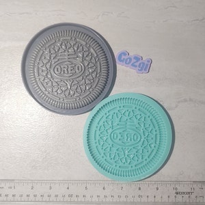 Op de afbeelding: Twee siliconen mallen voor het maken van Oreo-koekjes. De mallen zijn grijs en tealblauw en hebben het Oreo-logo en -ontwerp.