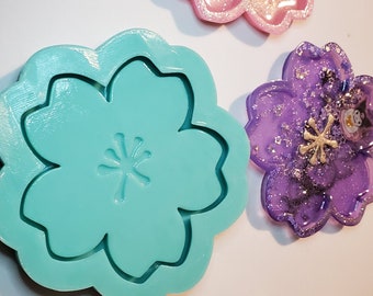 Può includere: Uno stampo in silicone color turchese a forma di fiore a cinque petali. Lo stampo ha un design in rilievo al centro.