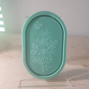 Può includere: Uno stampo in silicone verde chiaro a forma ovale con un design in rilievo di una farfalla e rose. Lo stampo è lungo circa 12,7 cm e largo 7,6 cm.