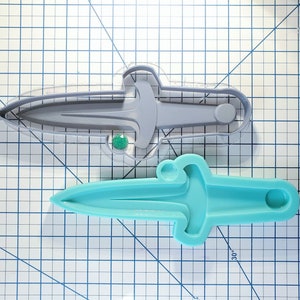 Könnte beinhalten: Zwei Silikonformen eines Dolches, eine grau und eine blaugrün. Die Formen befinden sich auf einer grauen, gerasterten Oberfläche.