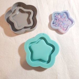 May include: Three star-shaped molds in the image. One is gray, with a star-shaped interior. Another is a light blue silicone mold. The third is a star-shaped pendant filled with small beads and glitter.