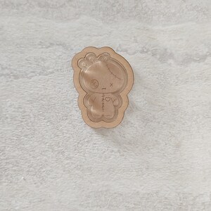 May include: A wooden cutout of a stitched doll with a heart on its chest. The doll has a stitched-up mouth and eyes.
