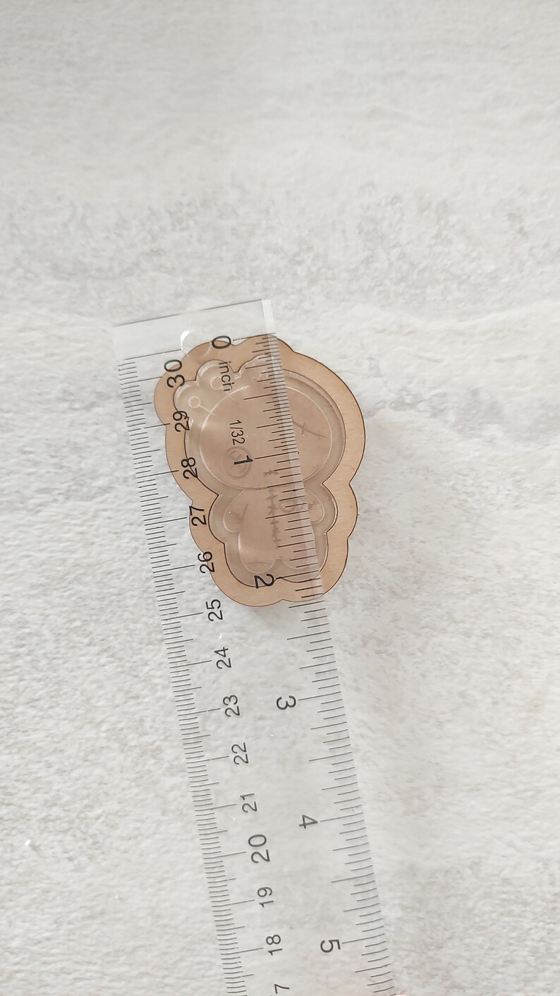 May include: A clear plastic bear-shaped mold for resin casting, measuring approximately 2 inches in diameter. The mold is placed on a ruler for size reference.