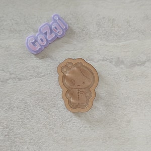 May include: A wooden cutout of a stitched doll with a heart on its chest. The doll has a stitched X for eyes and a stitched mouth. The cutout is on a light gray background.