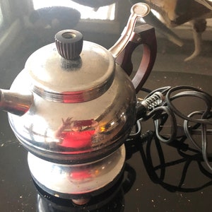 May include: A vintage chrome and brown electric coffee percolator with a cord and plug. The percolator has a round body with a handle and a lid.