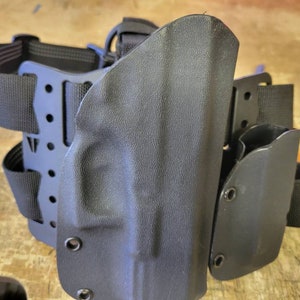 May include: Black tactical leg holster with adjustable straps and multiple attachment points. The holster is made of durable plastic and has a smooth, matte finish.