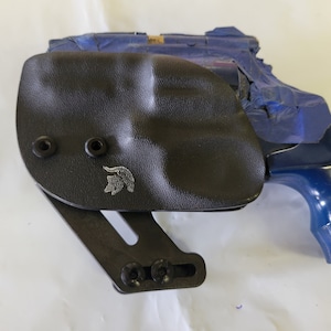 May include: A black leather holster with a silver logo and a blue revolver.