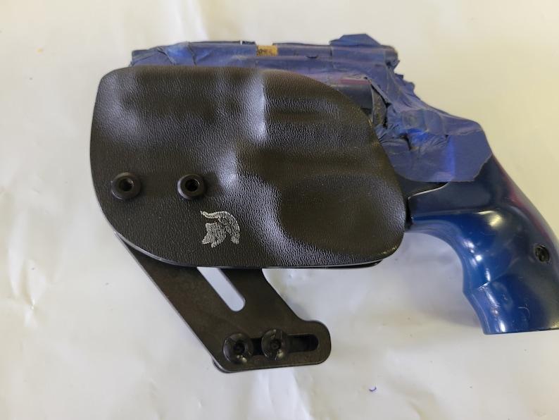 May include: A black leather holster with a silver logo and a blue revolver.