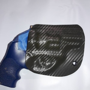Könnte beinhalten: Eine blaue Pistole mit einem schwarzen Kohlefaserholster. Das Holster hat ein kleines Loch oben rechts.