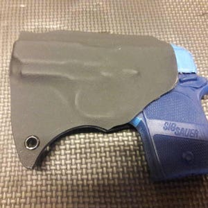 Puede incluir: Una funda de cuero negra con una pistola azul con el texto "SIG SAUER" en el lateral.