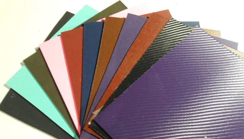May include: A fan of various colored leather and textured vinyl samples. Colors include black, teal, pink, red, brown, navy, purple, and carbon fiber. The samples are arranged in a semi-circular pattern, showcasing the different textures and hues.