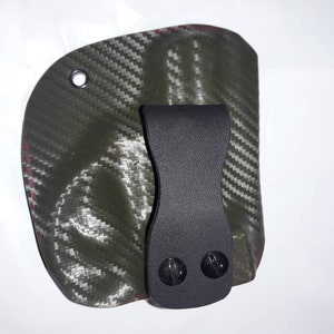 May include: A black leather holster with a carbon fiber pattern and a clip. The holster has two black screws on the clip.