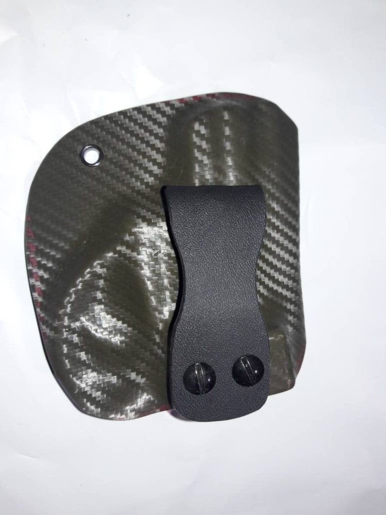 May include: A black leather holster with a carbon fiber pattern and a clip. The holster has two black screws on the clip.