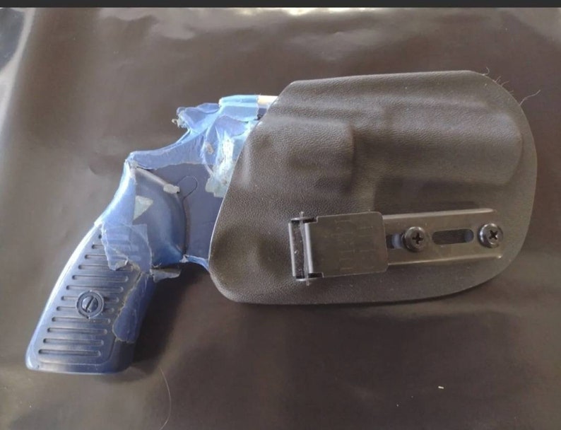May include: A blue handgun with a black holster. The handgun is partially covered in blue protective material. The holster is black and has a metal clip and screws.