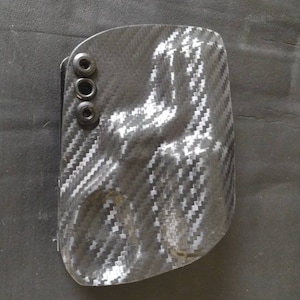 K&ouml;nnte beinhalten: Ein schwarzes und graues Holster aus Kohlefaser mit drei schwarzen Schrauben.