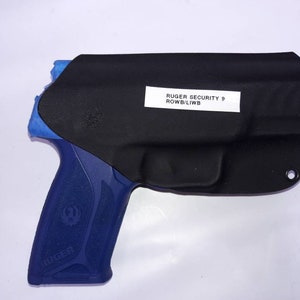 Peut inclure: Un &eacute;tui noir avec une arme de poing bleue. L'&eacute;tui porte une &eacute;tiquette indiquant "RUGER SECURITY 9 ROWB/LIWB". L'arme de poing est bleue avec le logo Ruger sur la poign&eacute;e. L'&eacute;tui est con&ccedil;u pour s'adapter &agrave; l'arme de poing.