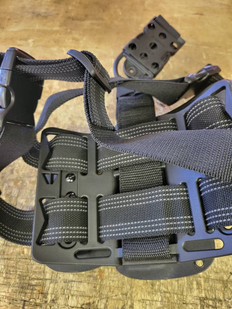 May include: Black tactical holster with adjustable straps and a belt loop. The holster is made of durable nylon and has a secure fit.