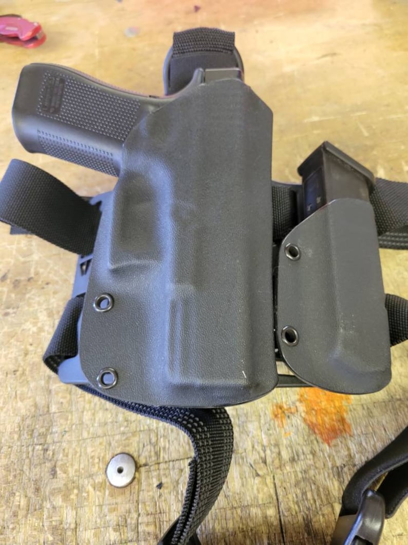 May include: A black tactical holster with a magazine pouch attached. The holster is made of a durable material and has a secure fit. The holster is designed to be worn on the hip or thigh.