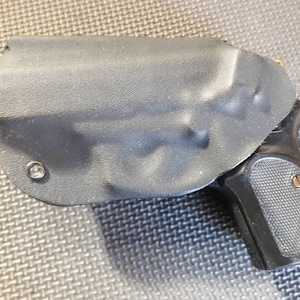 May include: A black leather holster with a black handgun inside. The holster has a snap closure and a metal rivet.