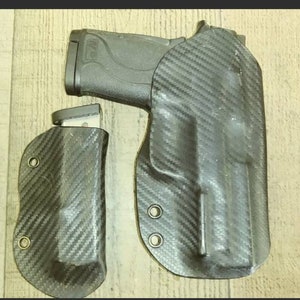 Peut inclure: Un pistolet noir avec un chargeur et deux étuis en fibre de carbone. Les étuis sont conçus pour contenir le pistolet et le chargeur en toute sécurité. La fibre de carbone présente un motif tissé.