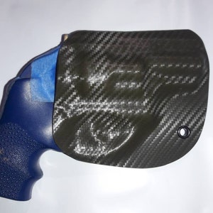May include: A black carbon fiber holster with a blue gun inside. The holster has a small hole on the top right side.