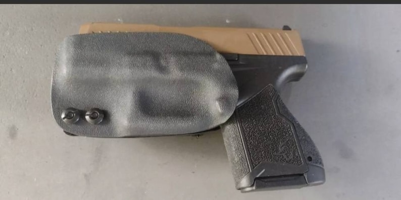 May include: A black and tan handgun with a black holster. The holster has two screws on the side.